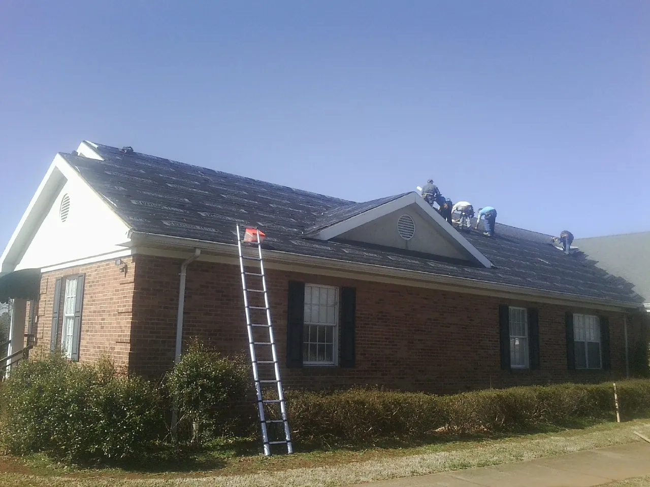 Crew tearing shingles off a brick ranch roof with a ladder set — Emergency Roof Repair work by our crew in Burr Oak