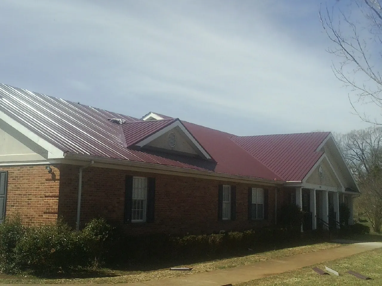 Red metal roof with gabled entries on a long brick building, from a Hail Damage Roof Repair job in Burr Oak