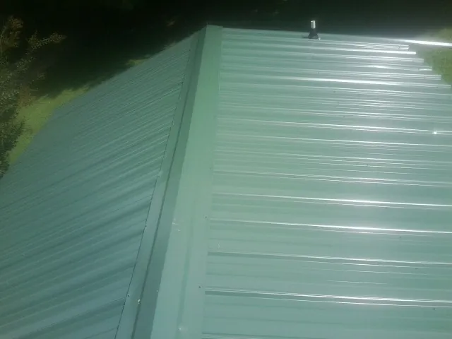 New green metal panels meeting at the ridge of a roof — Flat Roof Repair work by our crew in Burr Oak