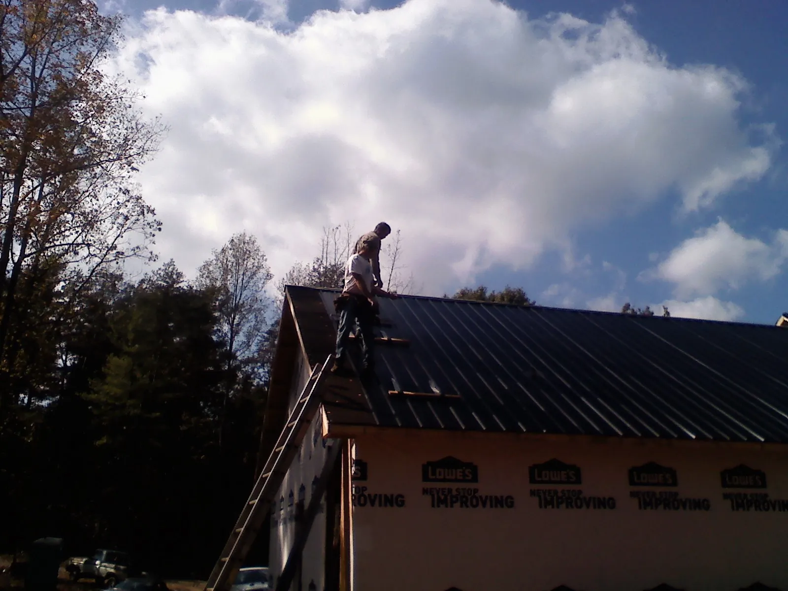 Roofer fastening dark metal panels high against a cloudy sky, from a Roof Inspection job in Burr Oak