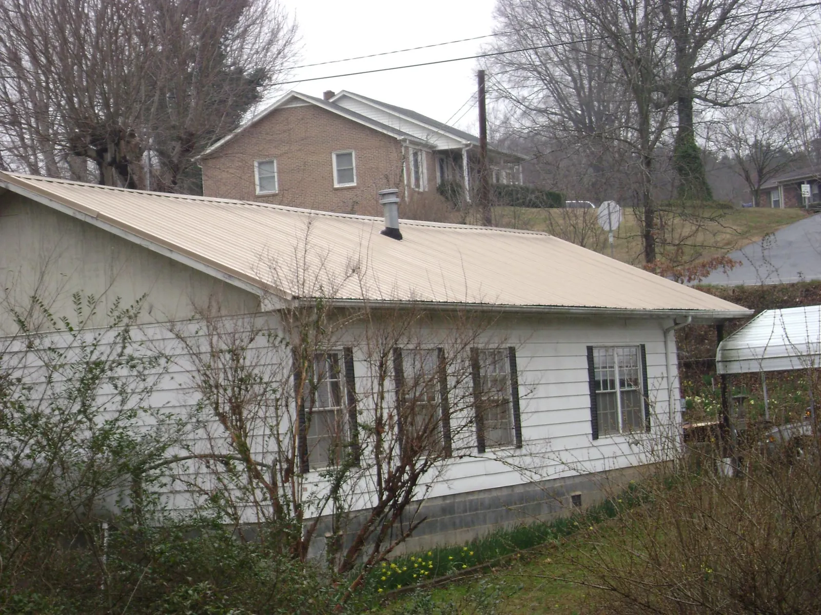 Tan metal roof on a white sided house set into a hillside — Commercial Roofing by Roofing Brothers in Burr Oak