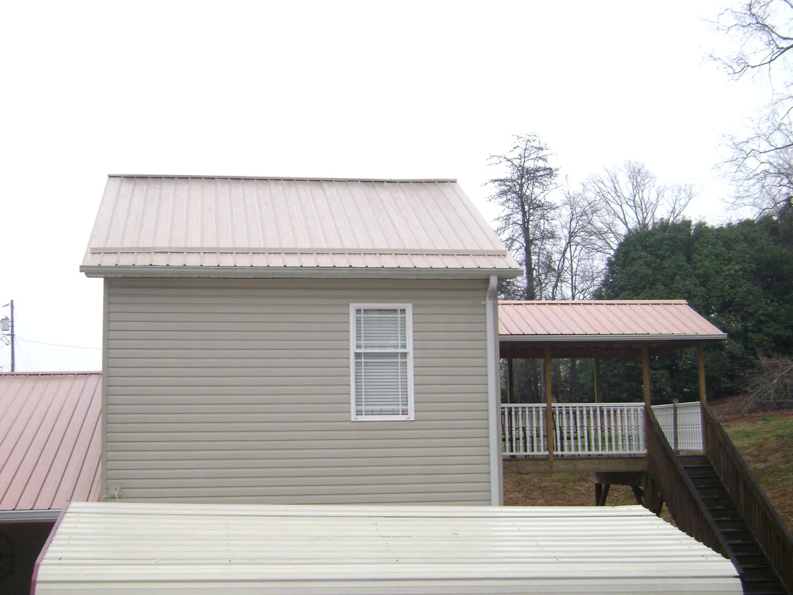 Tan metal roofs on a two story addition and attached porch, from a Roof Replacement job in Burr Oak